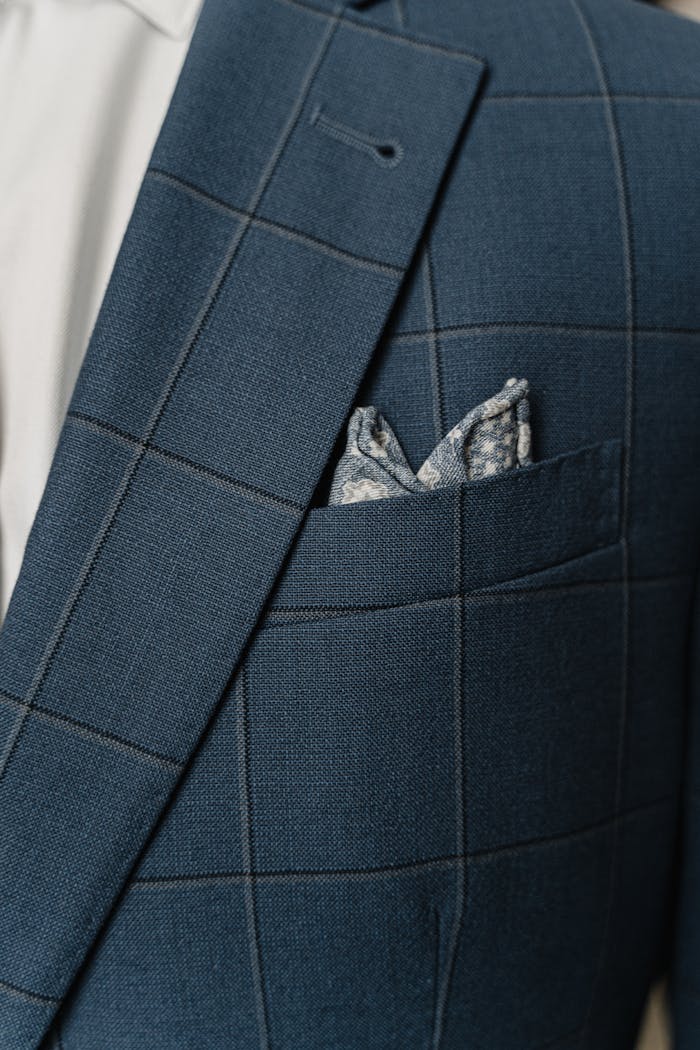 Close-up of an elegant blue checked suit jacket with a pocket square, showcasing fine tailoring.