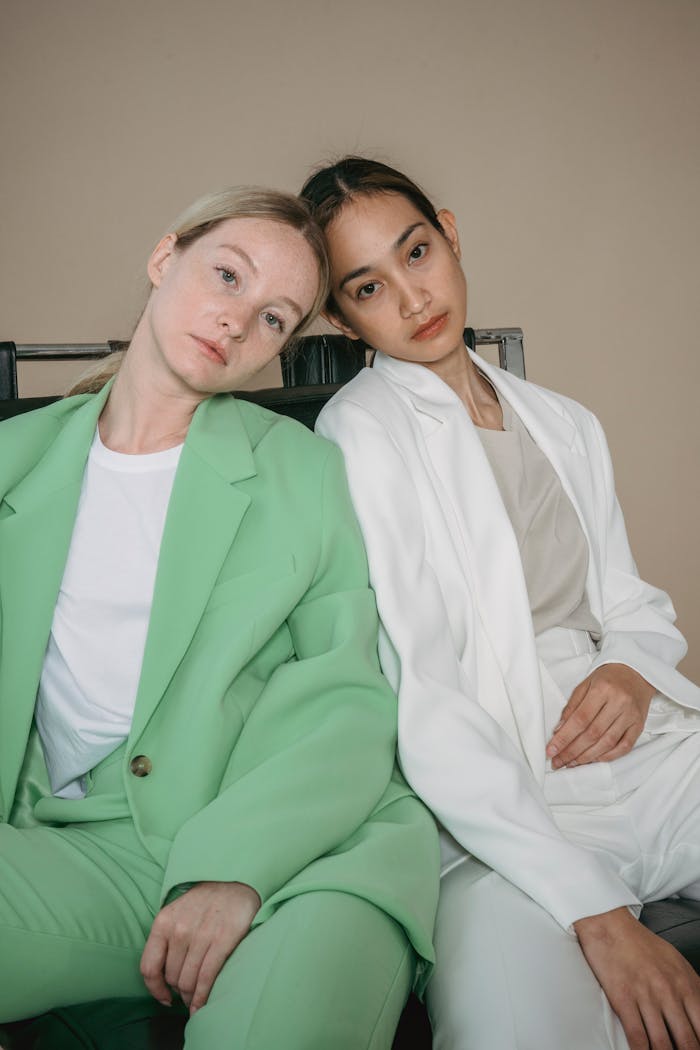 Two women in green and white blazers sitting closely. Modern fashion style.